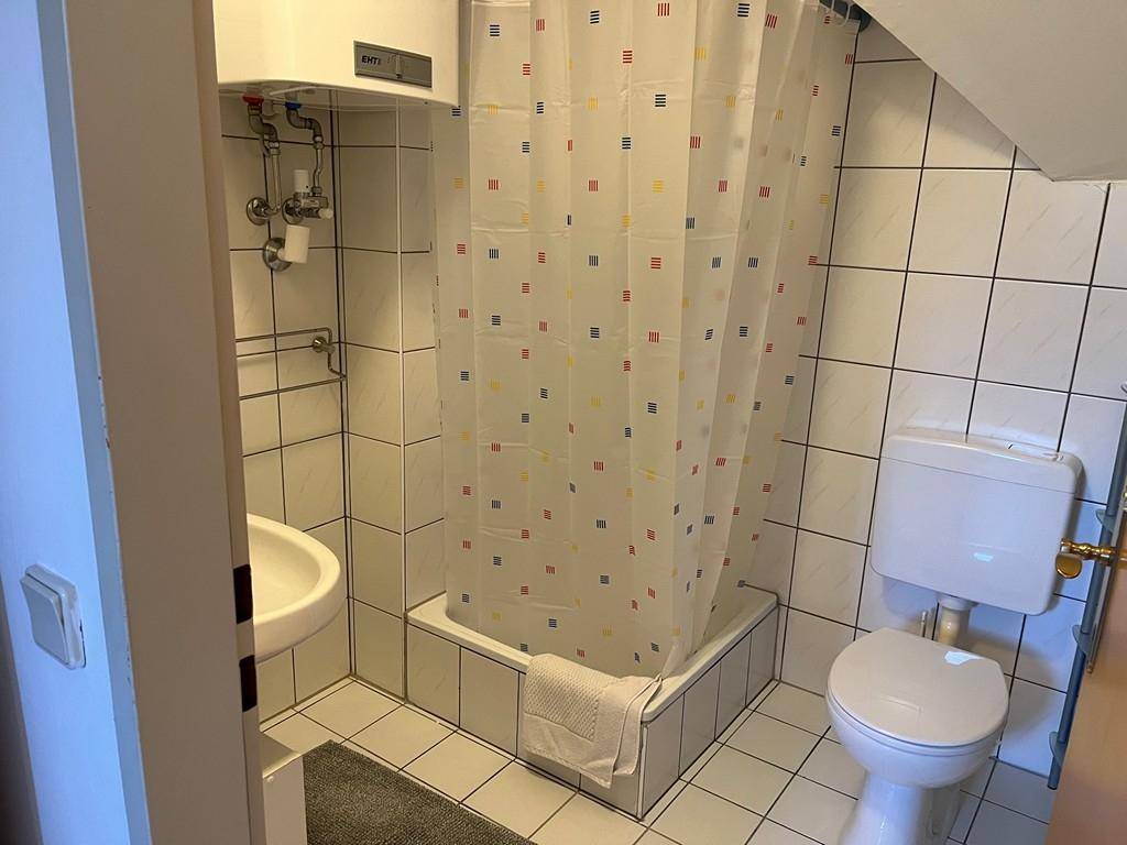 Badezimmer mit Dusche, WC, Waschbecken und weiß-blau-rotem Duschvorhang.