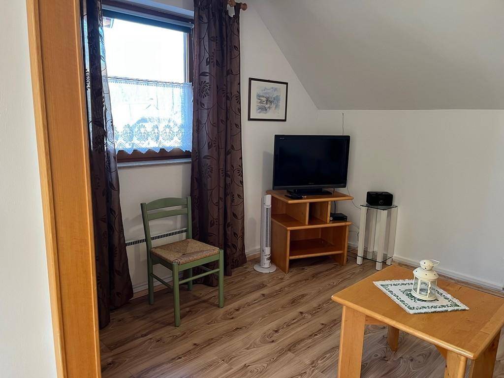 Wohnzimmer mit Fenster, Fernseher und Holzmöbeln.