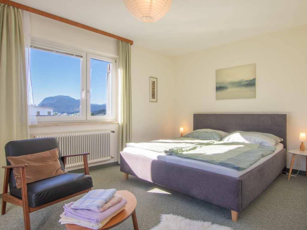 Ruhiges Schlafzimmer mit Doppelbett, Sessel und großem Fenster mit malerischem Bergblick.