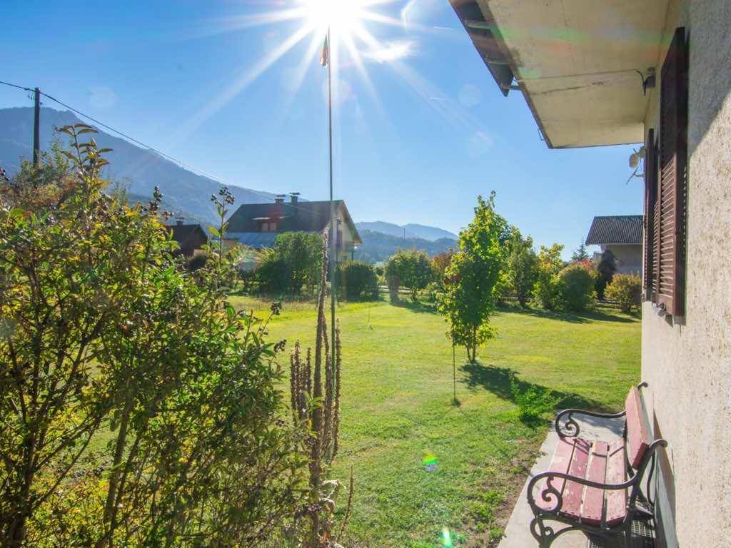 Sonniger Gartenbereich mit Sitzbank, grüner Wiese und Blick auf die umliegende Berglandschaft.