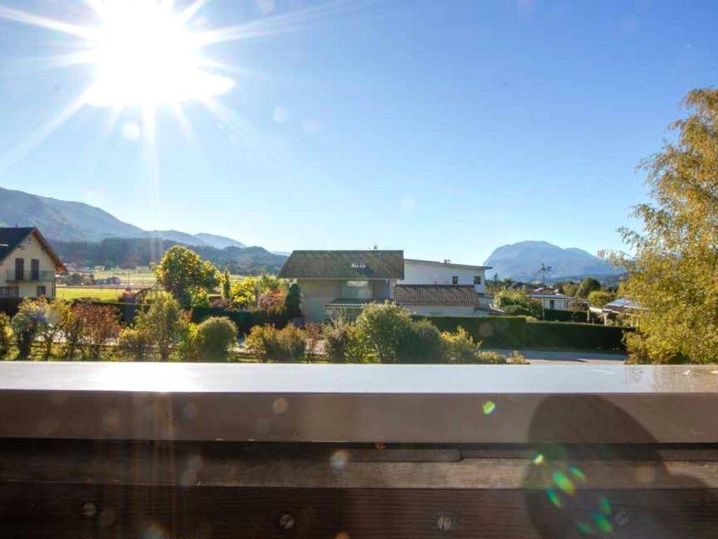 Sonniger Ausblick vom Balkon auf die grüne Umgebung mit Häusern und einer malerischen Bergkette.
