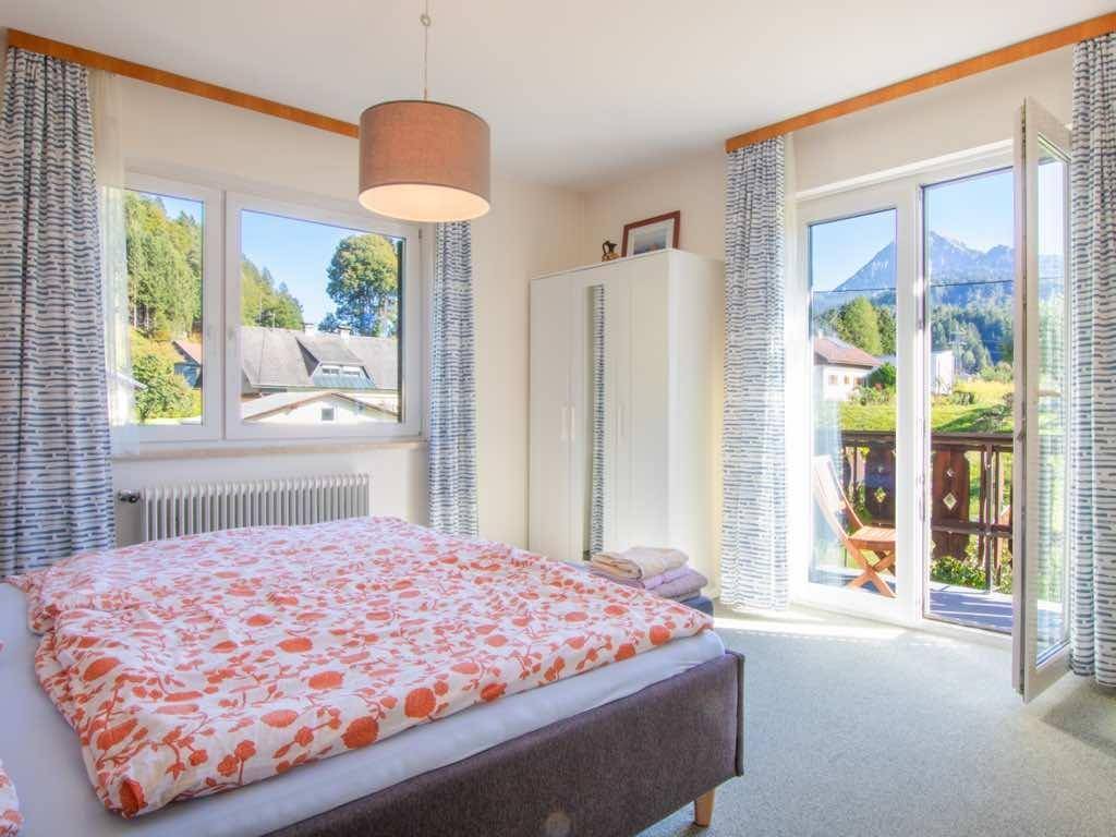 Helles Schlafzimmer mit Doppelbett, Kleiderschrank und Balkonzugang mit Bergblick.