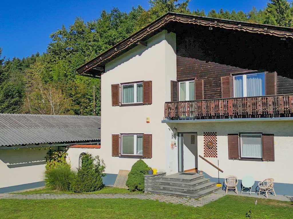 Charmante Hausfassade im Landhausstil mit Holzbalkon, Fensterläden und gepflegtem Vorgarten.