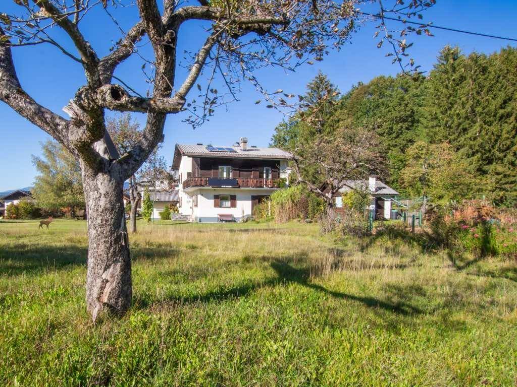 Traditionelles Haus umgeben von einer weitläufigen Wiese mit Obstbäumen und Bergblick.