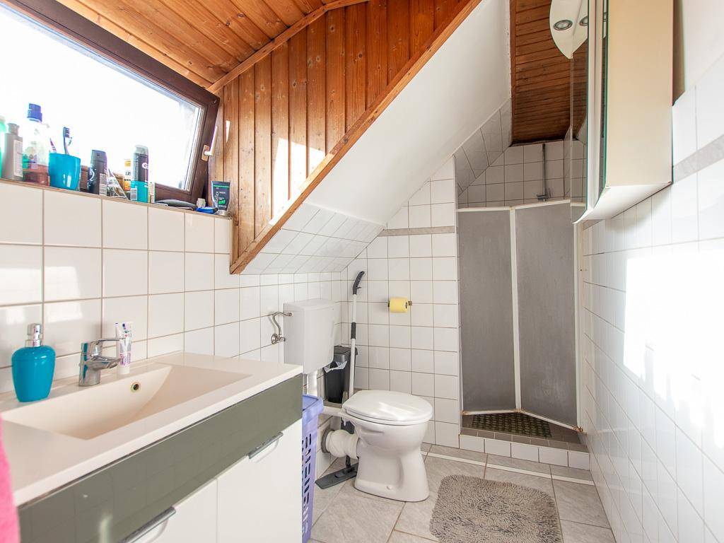 Badezimmer im Dachgeschoss mit Dusche, WC, Waschbecken und Holzverkleidung an der Decke.