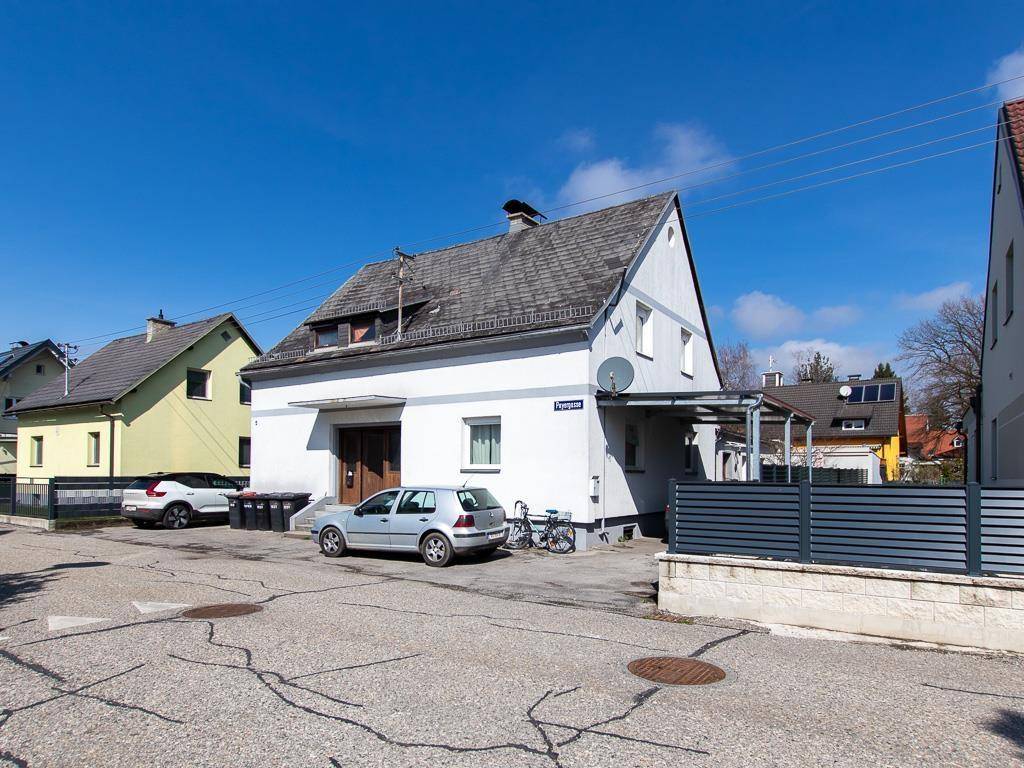 Einfamilienhaus mit Satteldach und Carport an einer ruhigen Wohnstraße unter blauem Himmel.