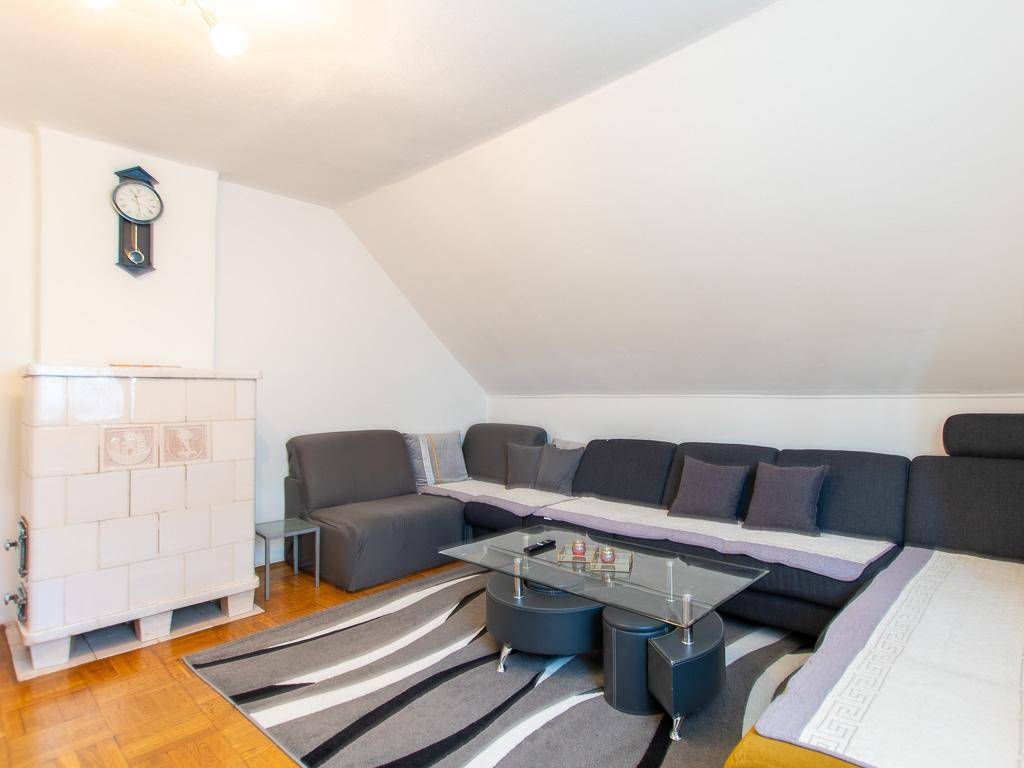 Gemütliches Wohnzimmer im Dachgeschoss mit Kachelofen, Sofa und Holzboden.