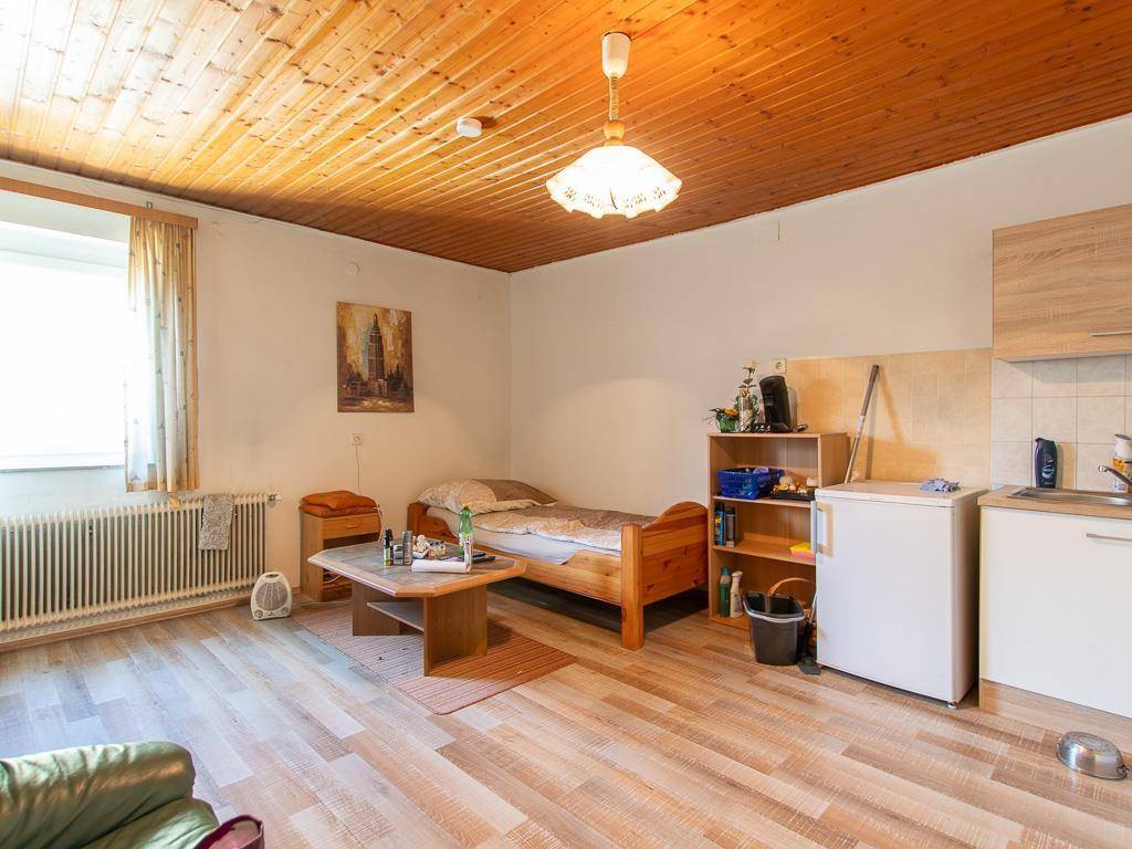 Einfaches Zimmer mit Bett, kleiner Küchenzeile und Holzboden, ideal als Gästezimmer.