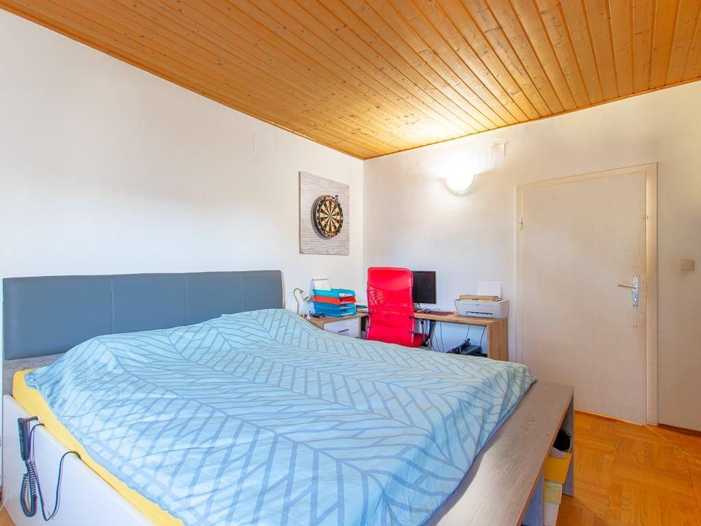 Schlafzimmer mit Holzbalkendecke, Bett und einem kleinen Schreibtischbereich.