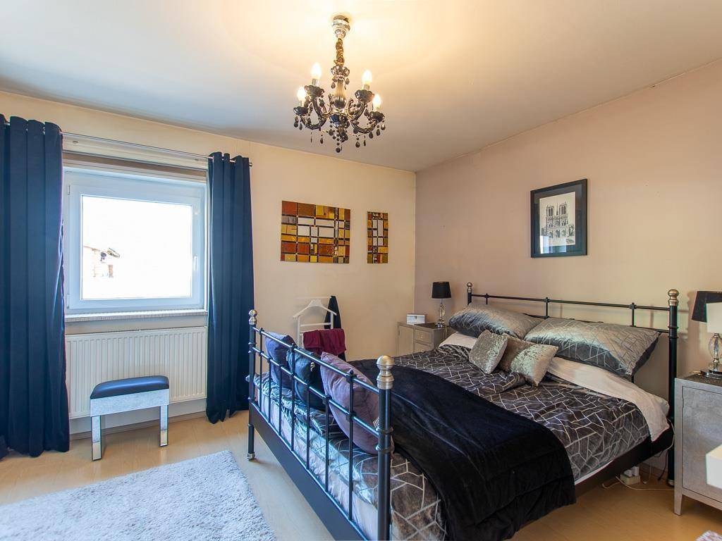 Schlafzimmer mit Doppelbett, dunklen Vorhängen und einem Kronleuchter an der Decke.