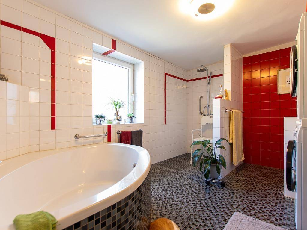 Geräumiges Badezimmer mit Badewanne, Dusche, weißen und roten Fliesen sowie einem Fenster.