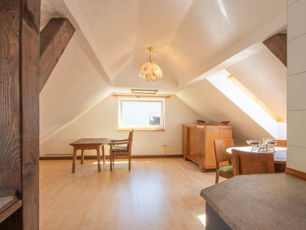 Geräumiges Wohnzimmer im Dachgeschoss mit Holzboden, sichtbaren Balken und viel Tageslicht.