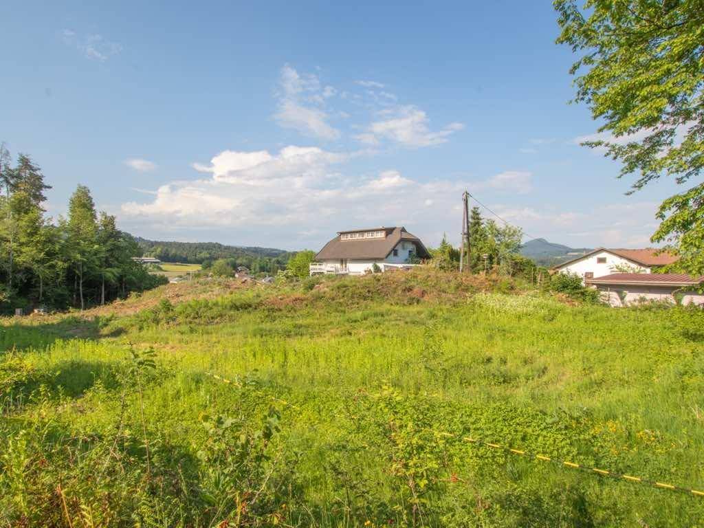 Grünes Feld mit einem Haus auf einem Hügel und Bergen im Hintergrund unter blauem Himmel.