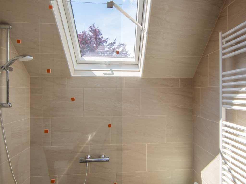 Modern gefliestes Badezimmer mit Dusche, Dachfenster und Handtuchheizkörper.
