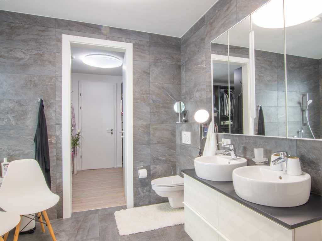 Modernes Badezimmer mit grauen Fliesen, Doppelwaschbecken und Spiegelschrank.