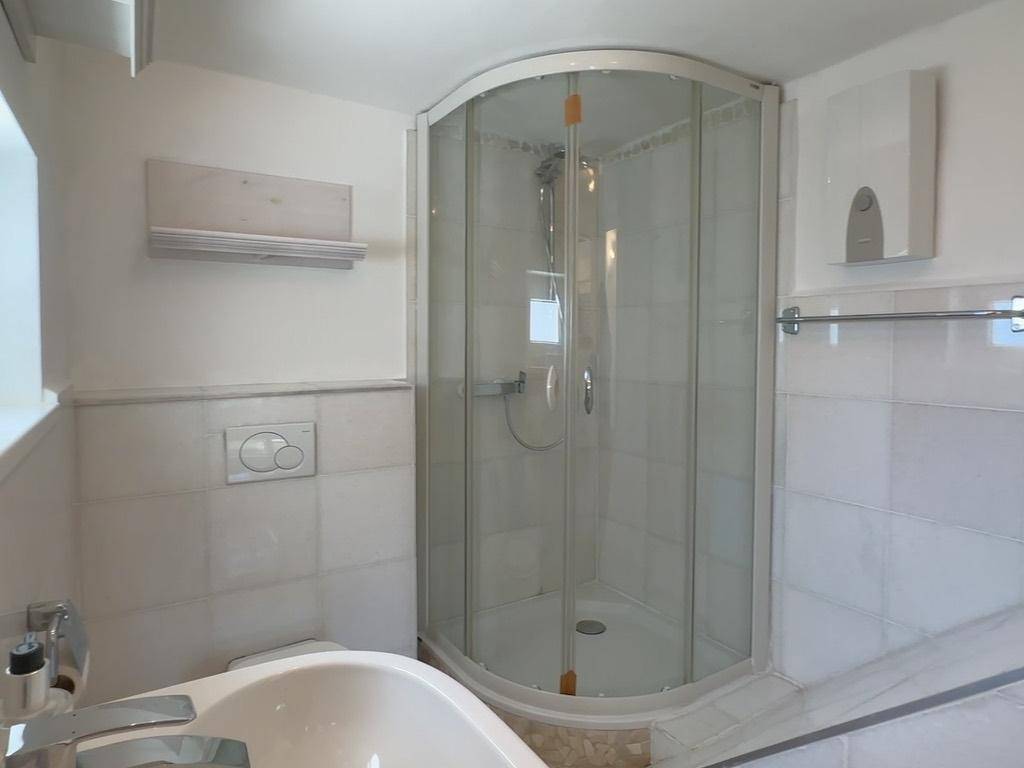 Helles Badezimmer mit Duschkabine, Waschbecken und weißen Fliesen.