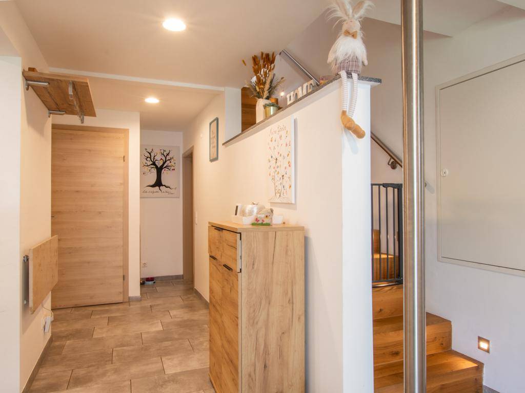 Heller Flur mit modernen Fliesen, Holzmöbeln und Zugang zur Treppe.