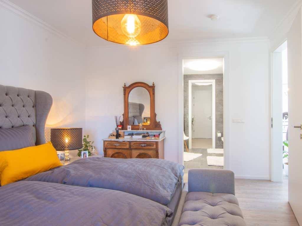 Schlafzimmer mit stilvollem Bett, Kommode und Blick auf das angrenzende, hell geflieste Badezimmer.