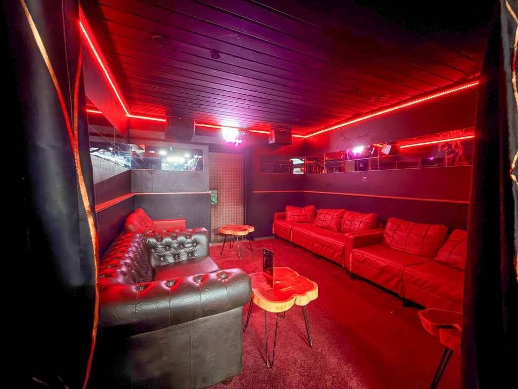 Geräumiger Lounge-Bereich mit mehreren Ledersofas, kleinen Tischen und stimmungsvoller roter Beleuchtung.