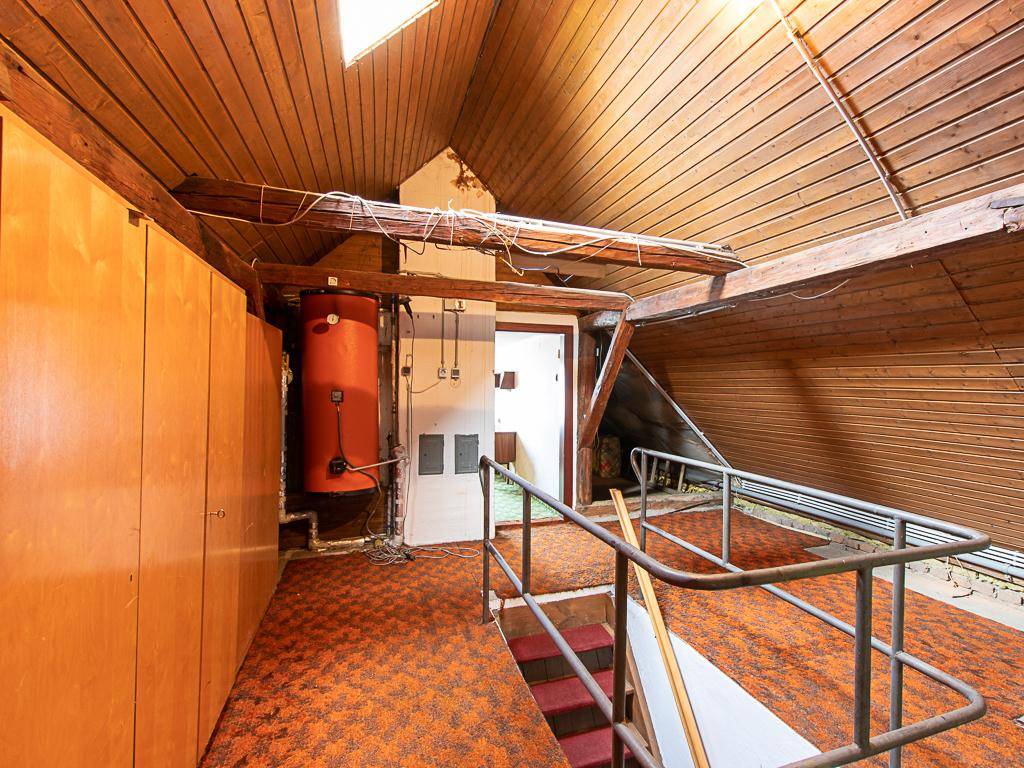 Geräumiger Dachboden mit sichtbaren Holzbalken, Teppichboden und Warmwasserspeicher.