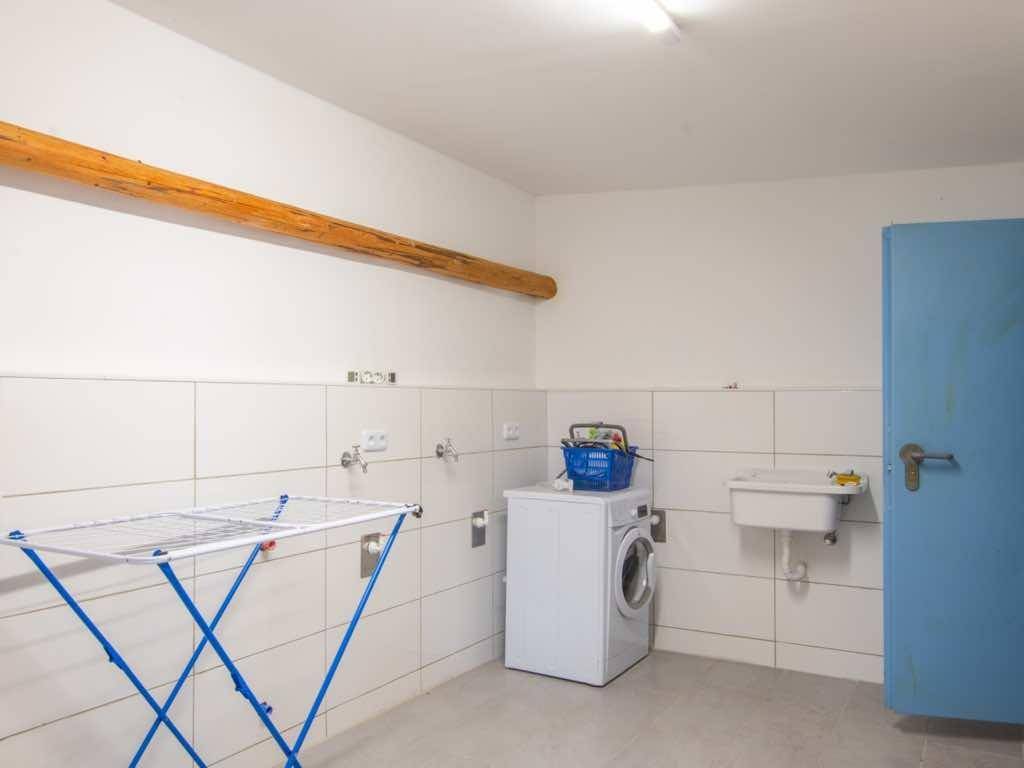 Funktionaler Hauswirtschaftsraum mit Waschmaschine, Waschbecken und Fliesenboden.