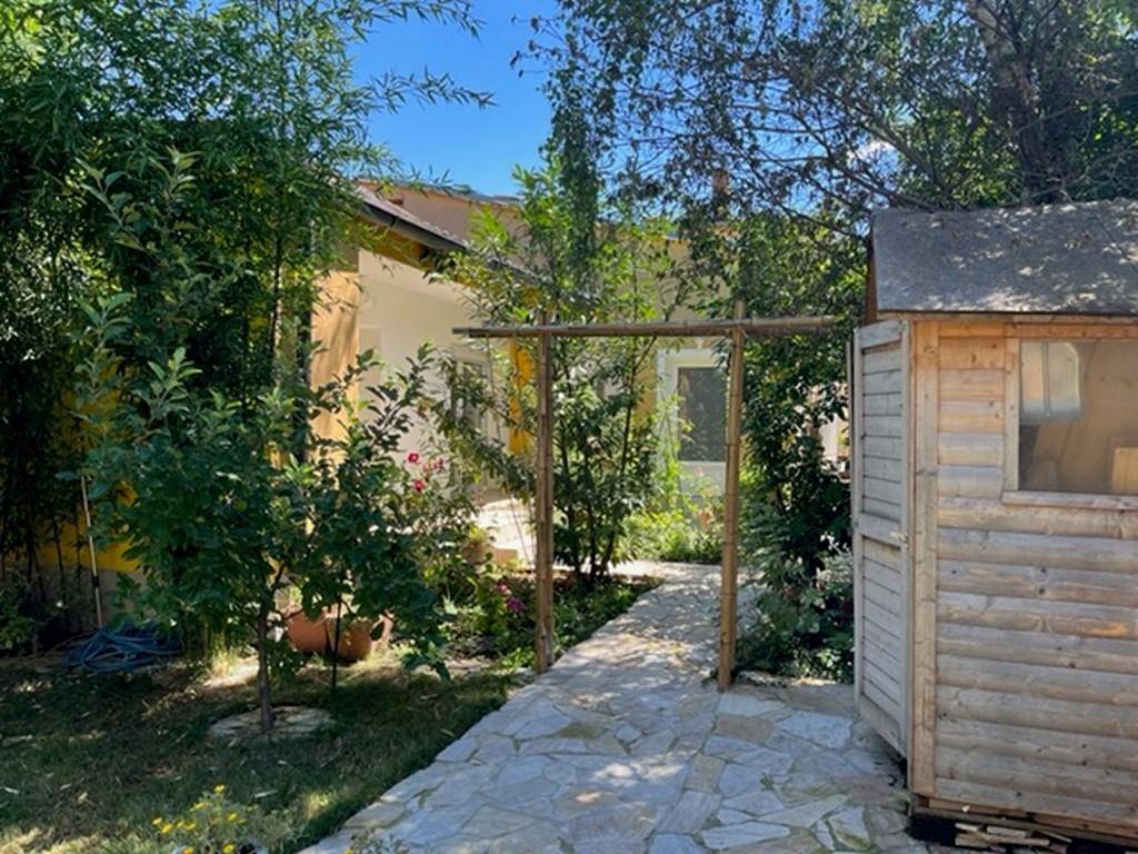 Grüner Garten mit Steinplattenweg, Bäumen und einem kleinen Holzschuppen.