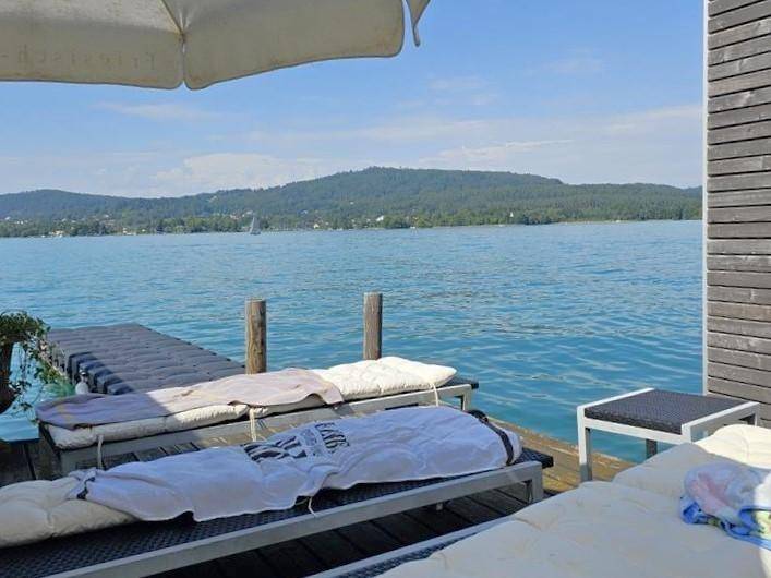 Entspannungsbereich auf der Holzterrasse mit Sonnenliegen und direktem Blick auf den See.
