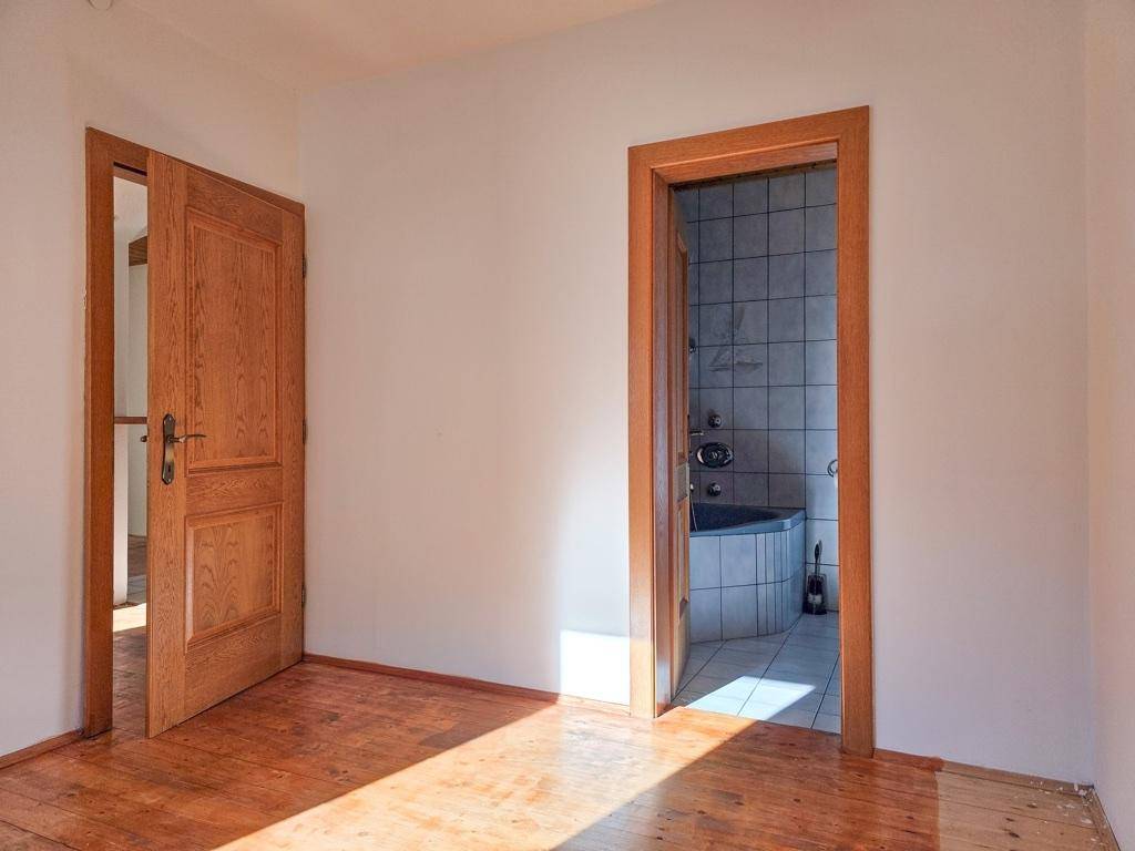 Heller Raum mit Holzboden und Zugang zu einem Badezimmer, ideal als Schlafzimmer.