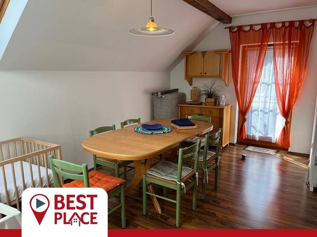 Rustikaler Essbereich mit Holztisch, grünen Stühlen, sichtbaren Balken und Zugang zum Balkon.