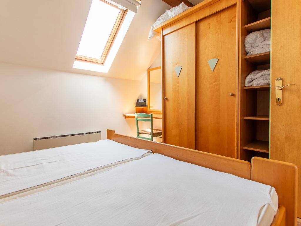 Schlafzimmer mit großem Holzschrank, Schreibtisch und Dachfenster, ideal für Gäste oder Kinder.