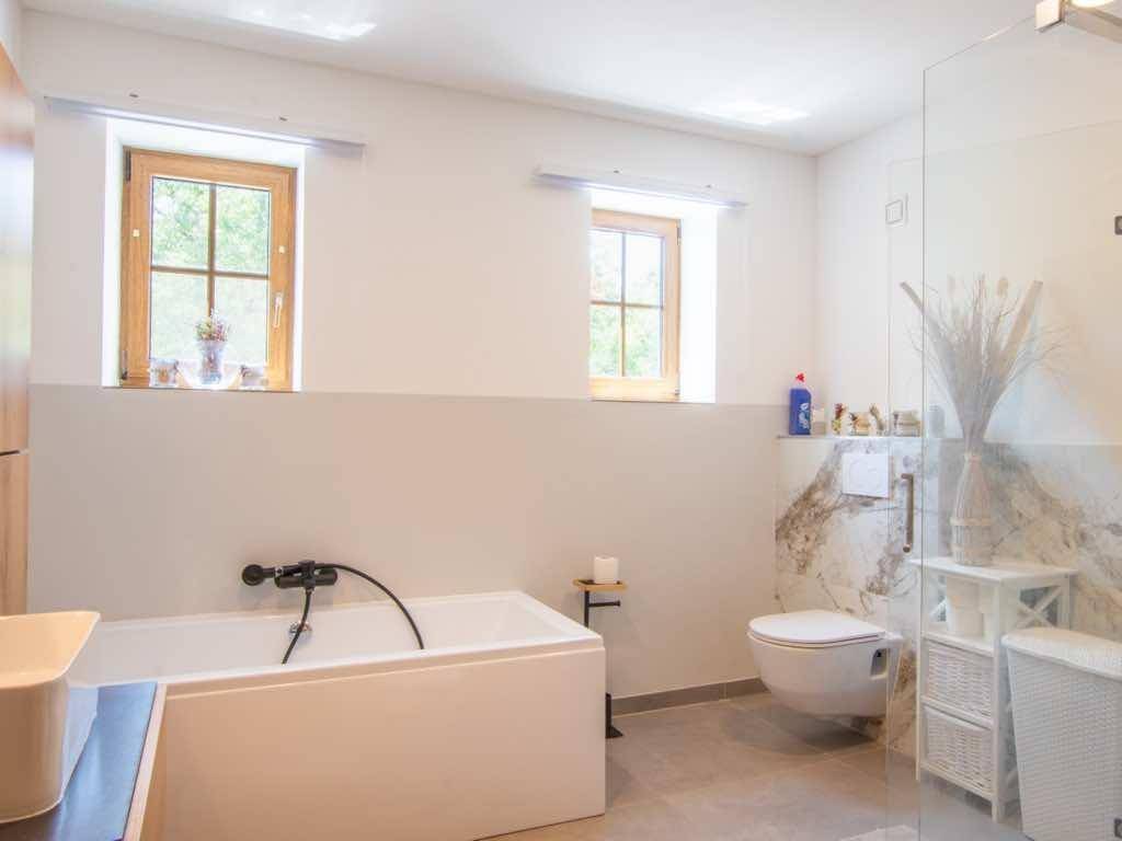 Modernes Badezimmer mit Badewanne, wandhängendem WC und begehbarer Dusche, hell durch Fenster.