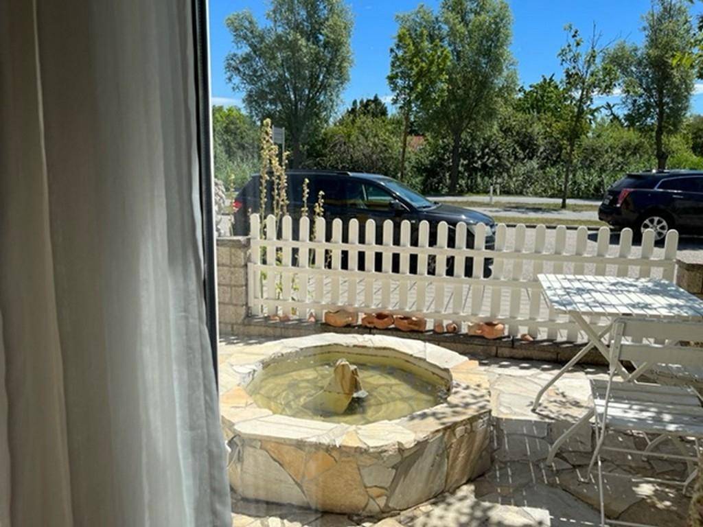 Blick aus dem Innenraum auf einen kleinen Außenbereich mit Brunnen und weißem Lattenzaun.
