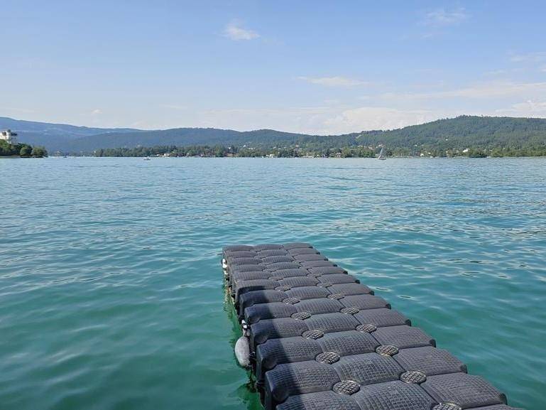 Schwimmender Steg auf dem See mit klarem Wasser und malerischer Berglandschaft im Hintergrund.