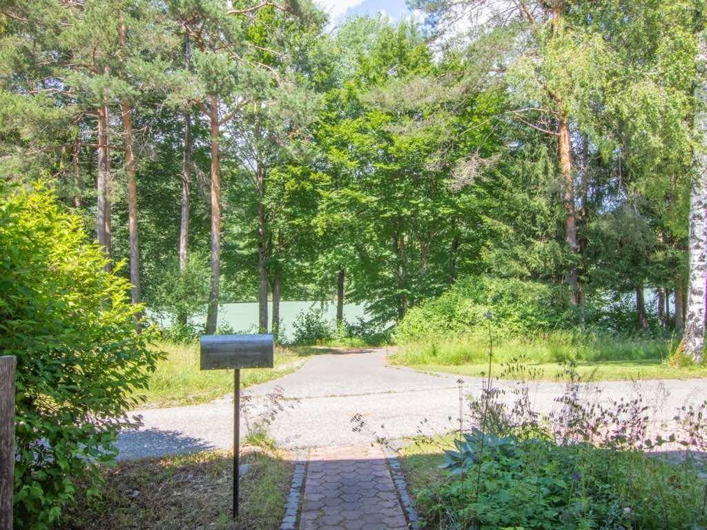 Gepflasterter Weg führt durch grüne Vegetation zu einem See im Hintergrund, mit einem Briefkasten am Rand.