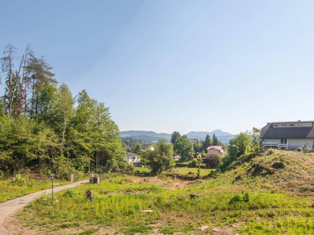 Weitläufiges, unbebautes Grundstück mit Blick auf umliegende Wälder, Häuser und ferne Berge.