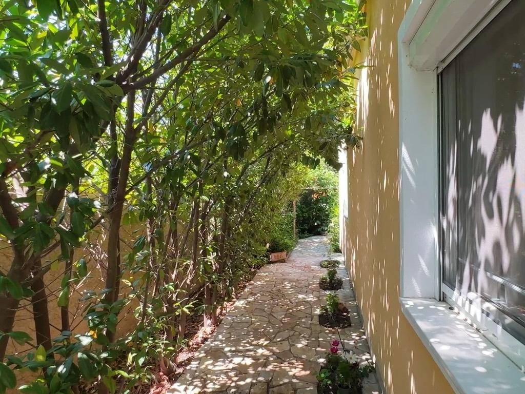 Schattiger Gartenweg mit Steinplatten, umgeben von hohen Hecken und Bäumen.