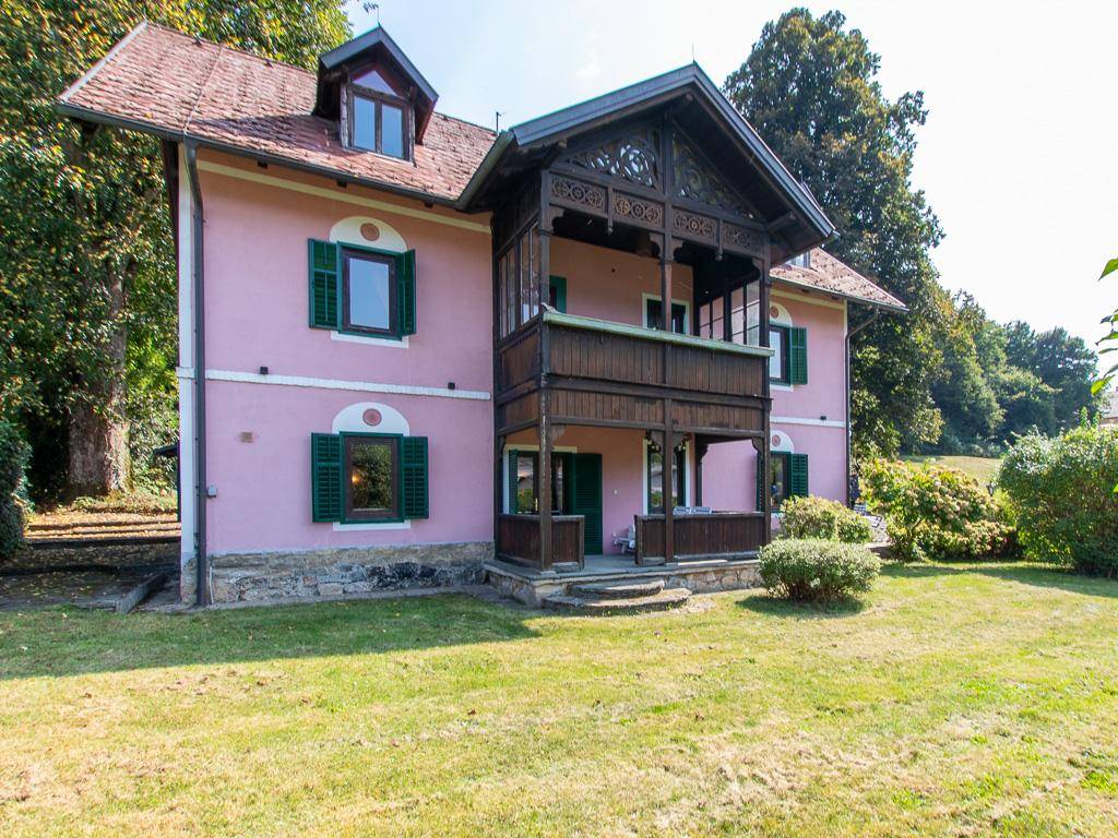 Seitliche Ansicht des rosa Hauses mit einem großen, kunstvoll geschnitzten Holzbalkon.