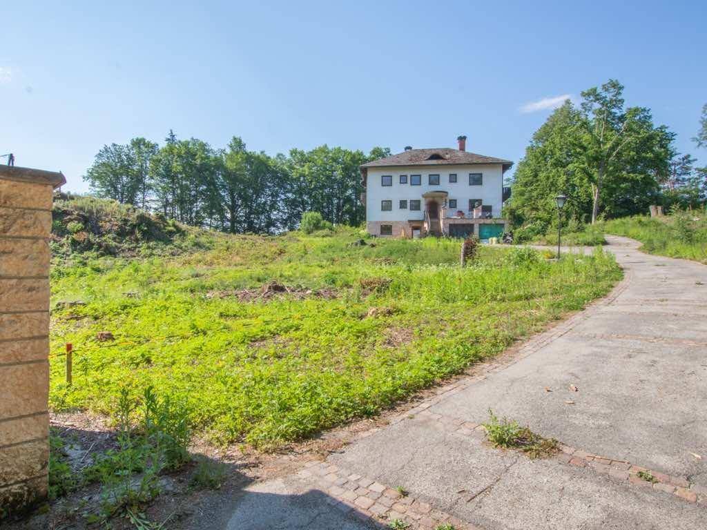 Unbebautes Grundstück mit einer großen weißen Villa im Hintergrund und einem gepflasterten Zufahrtsweg.