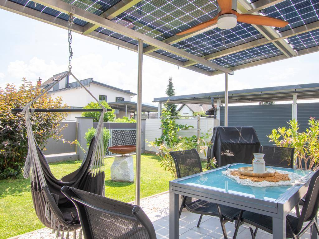 Überdachte Terrasse mit Solarpaneelen, Esstisch und Hängesessel im Garten.
