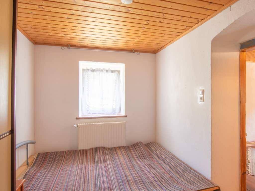 Kleines Schlafzimmer mit Bett, Fenster und einer gemütlichen Holzdecke.
