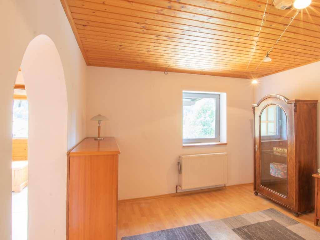 Heller Raum mit Holzdecke, Kommode und Vitrine, durch ein Fenster gut belichtet.