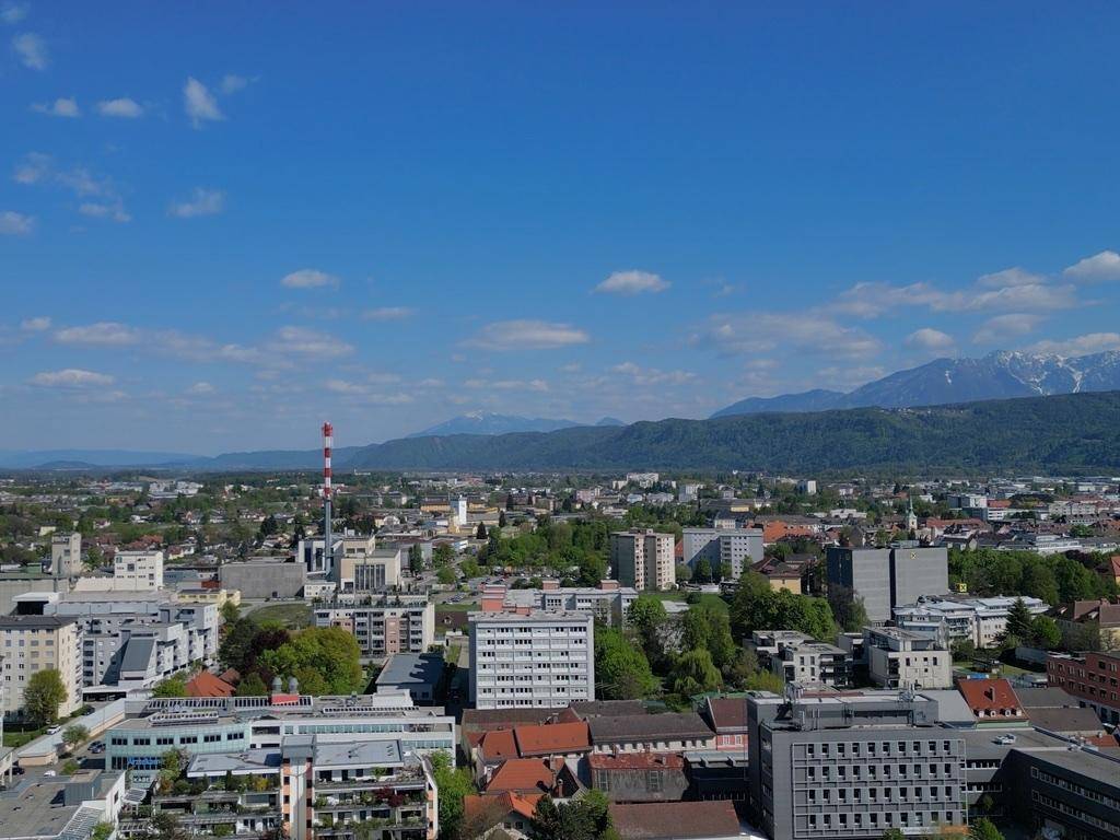 Weitläufiger Blick über die Stadtlandschaft mit Bergen im Hintergrund unter blauem Himmel.