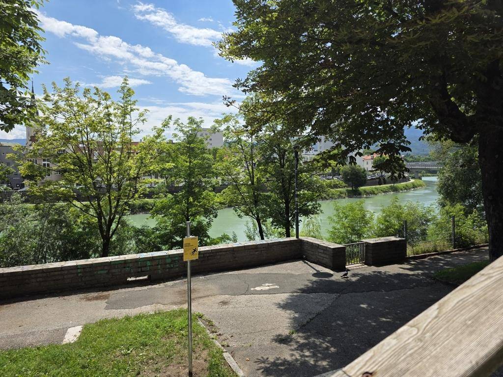 Außenbereich mit gepflastertem Weg und Blick auf den Fluss, umgeben von üppigem Grün.