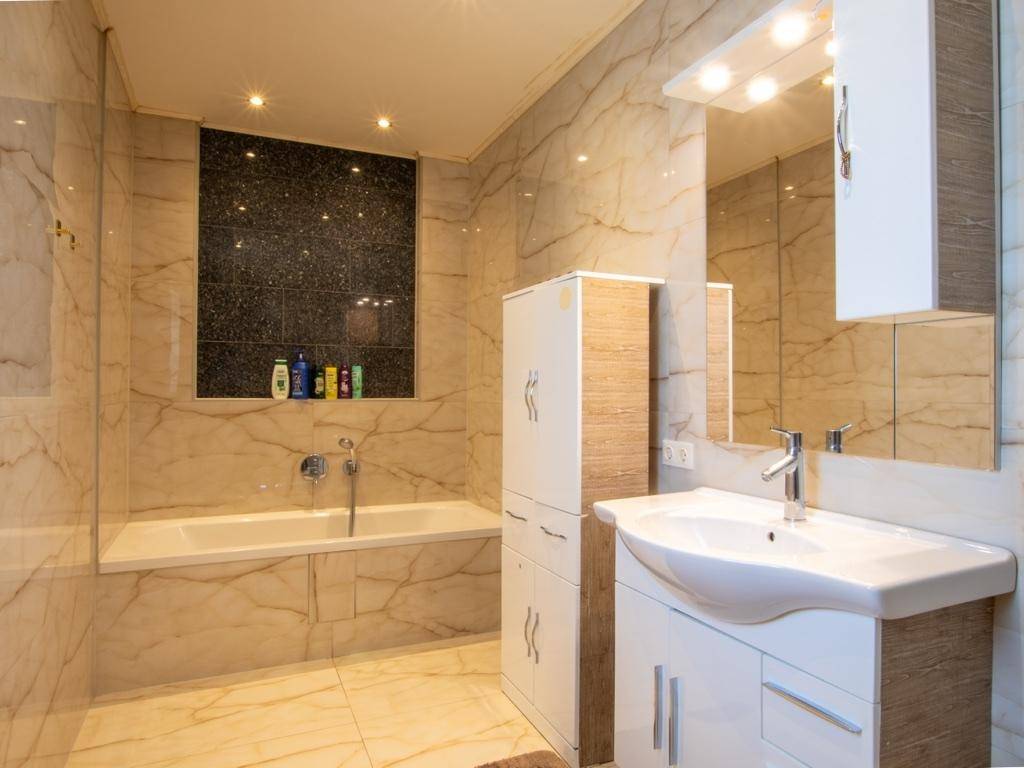 Modernes Badezimmer mit Marmoroptik-Fliesen, Badewanne und elegantem Waschtisch.