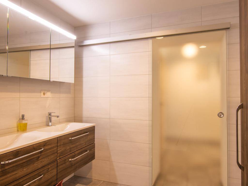 Modernes Badezimmer mit Einzelwaschbecken, Spiegelschrank und Milchglas-Schiebetür.