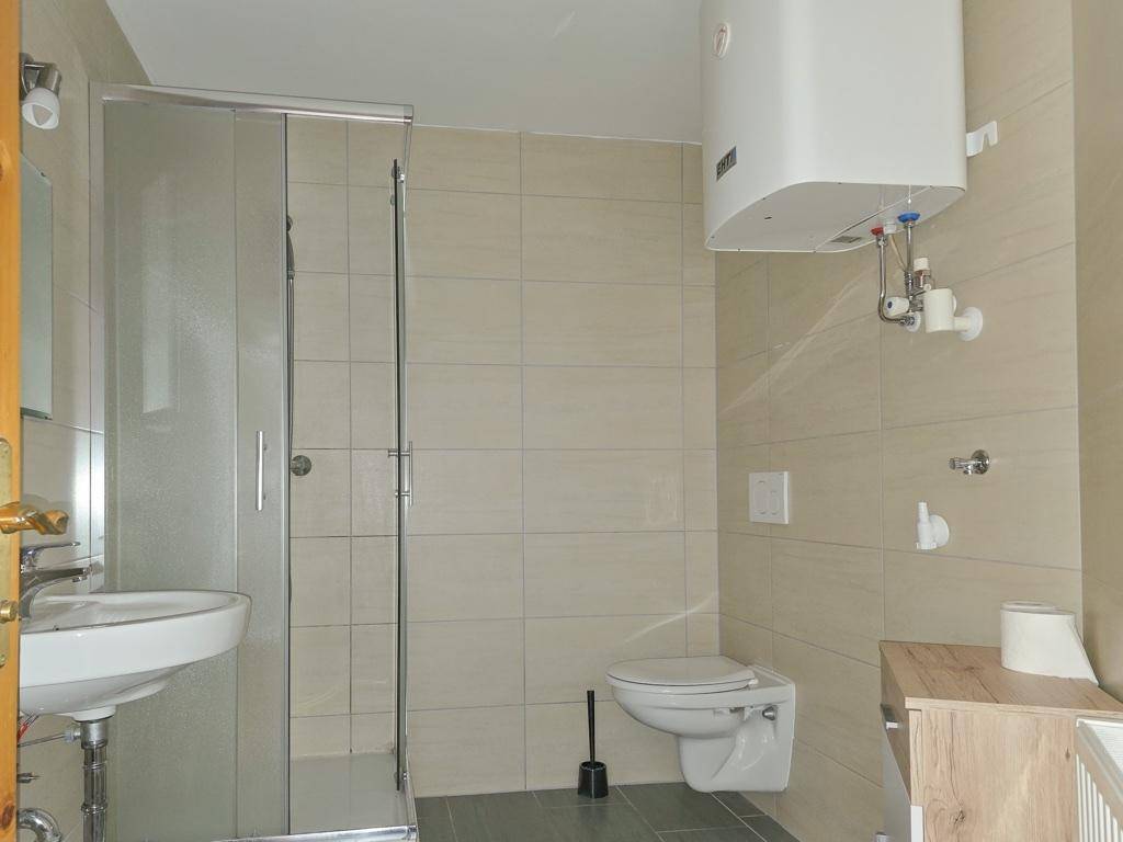 Modernes Badezimmer mit Duschkabine, wandhängendem WC und hellen Fliesen.