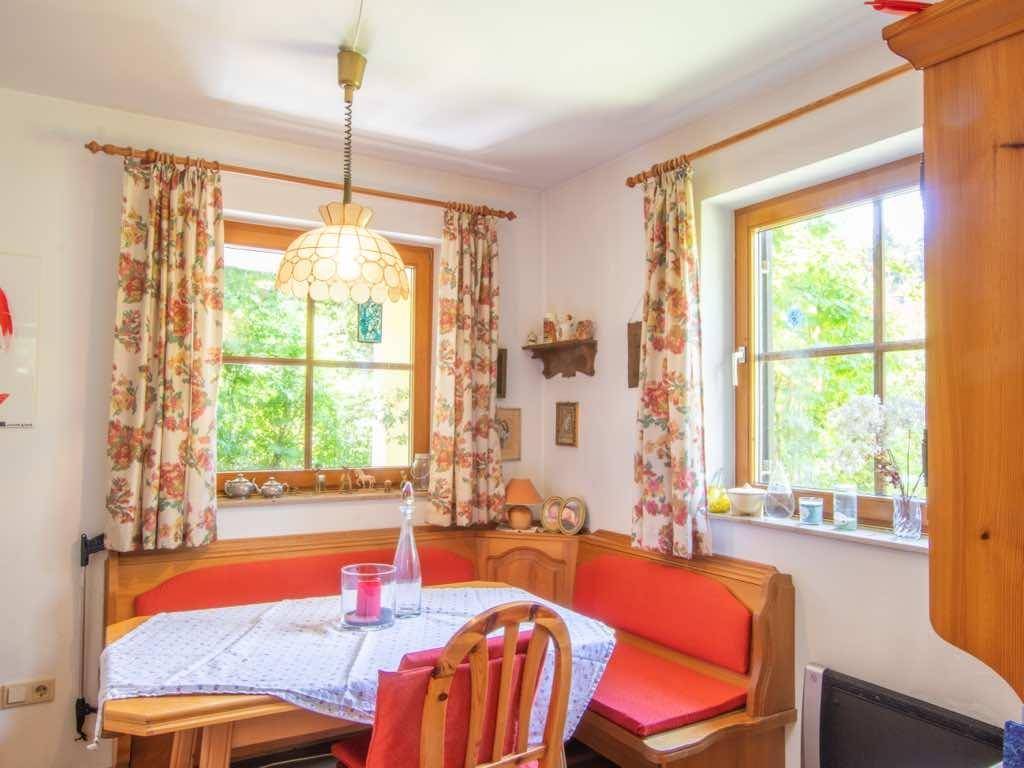 Gemütliche Essecke mit Holzbänken, Tisch und floralen Vorhängen, hell durch Fenster.
