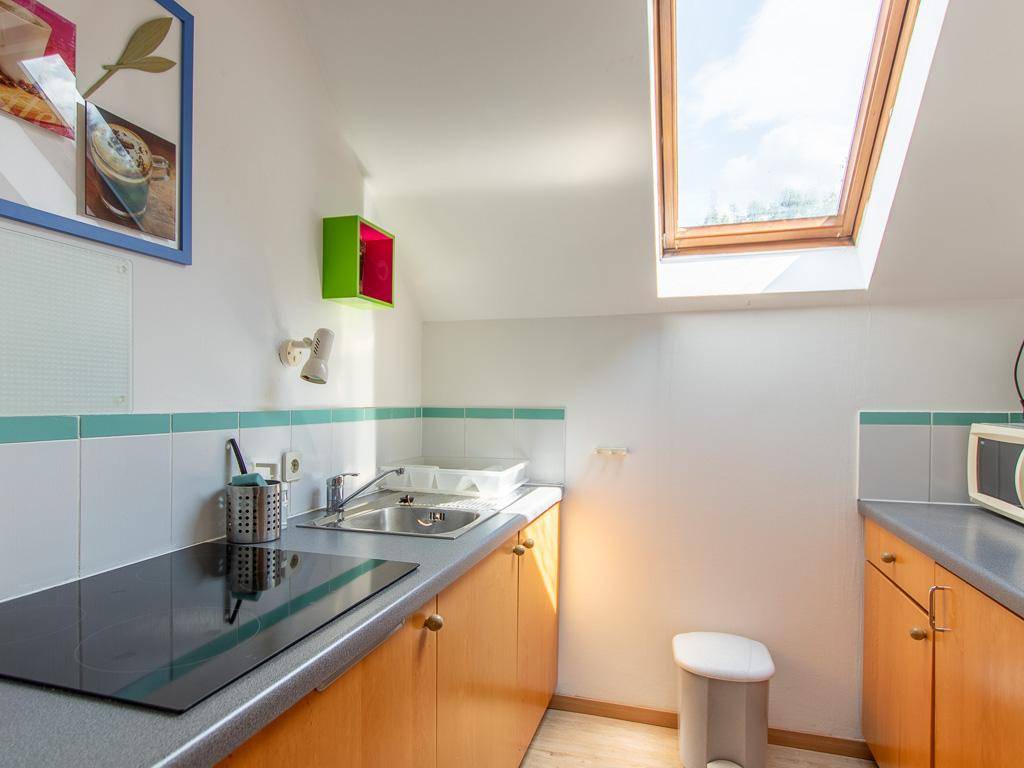 Helle Küchenzeile im Dachgeschoss mit Dachfenster, Spüle und Kochfeld.