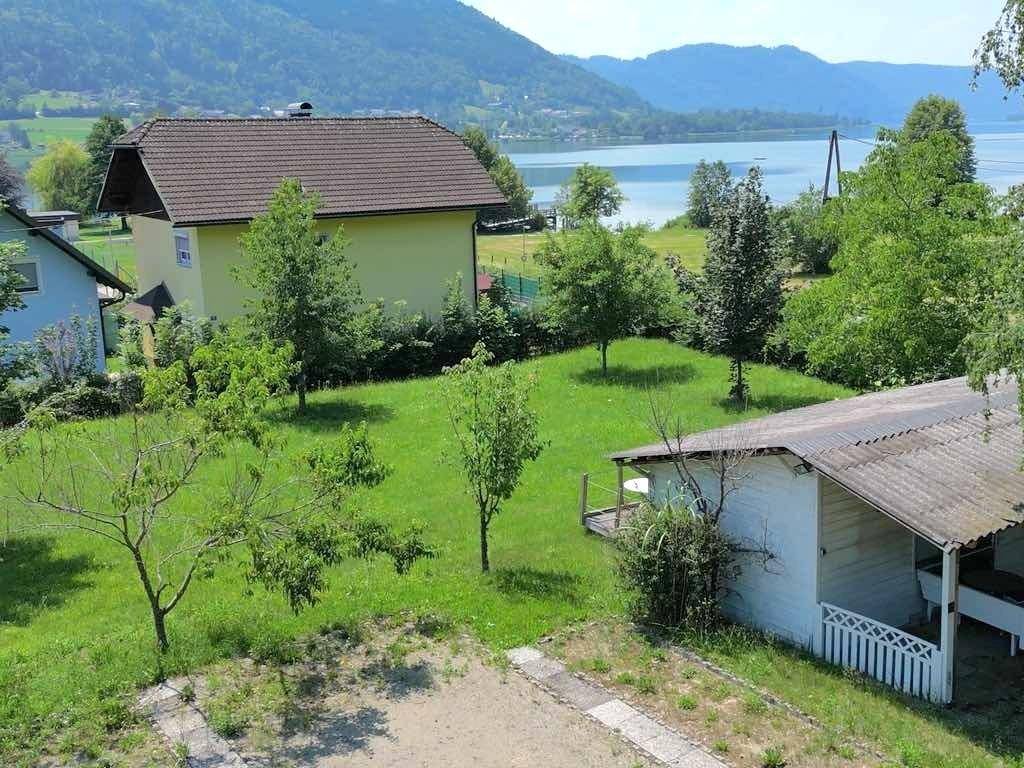 Grüne Gartenfläche mit einem kleinen Nebengebäude und Blick auf den See im Hintergrund.