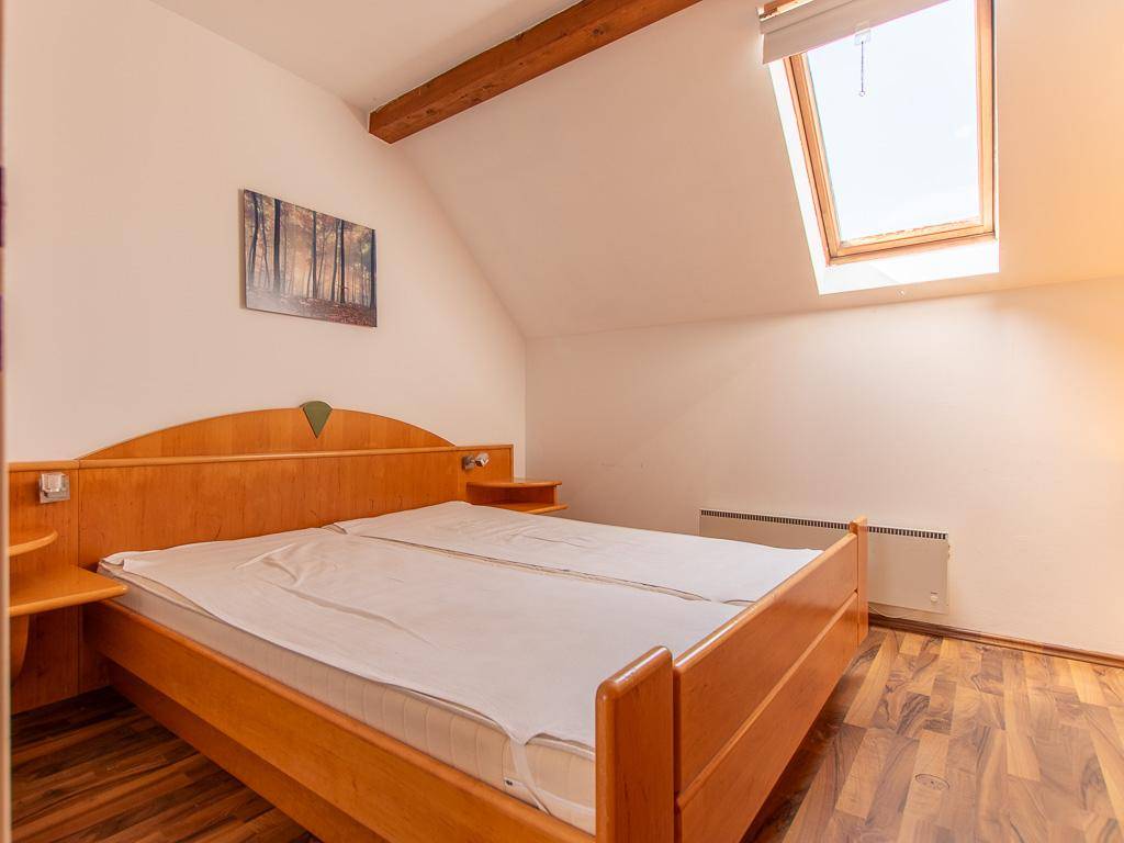 Schlafzimmer im Dachgeschoss mit Doppelbett, Holzbalken und großem Dachfenster.